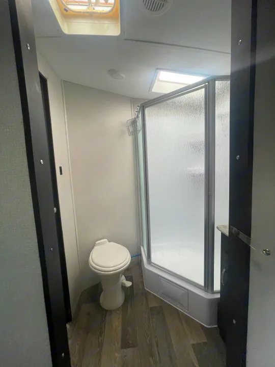 RV rental bathroom with compact toilet, frosted glass corner shower, and roof vents. Designed for efficient on-the-go living.. Keystone RV Springdale 2020
