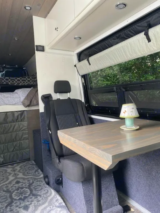 Inside a versatile RV rental camper van: Features a compact dining area with table, seating, & an inviting bed for travel comfort.. Mercedes Sprinter 2012