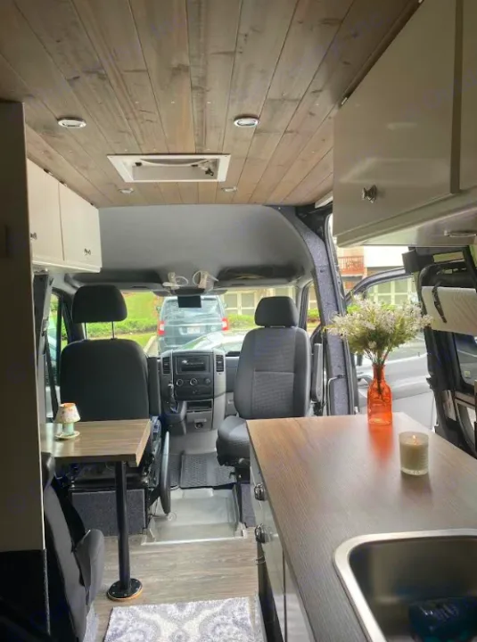 Spacious RV rental interior featuring a modern wood ceiling, kitchenette, seating area, and cozy accents. Perfect for mobile adventures.. Mercedes Sprinter 2012