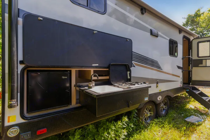 This RV rental's exterior features an open outdoor kitchen with a black mini-fridge, white sink, and two-burner stove.. North Trail 24bhs 2021