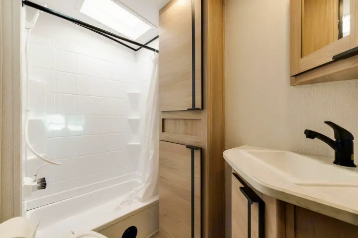 This RV rental's bright bathroom features a full shower, compact sink, and natural wood-look storage cabinets.. North Trail 24bhs 2021