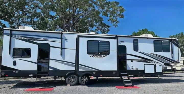 Spacious white Rogue Armored RV rental parked on gravel, featuring black and gray graphics and multiple slide-outs.. Forest River Vengeance Rogue Armored Toy Hauler 2021