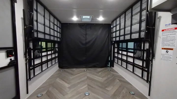 Inside an **RV rental** toy hauler: versatile garage space with fold-down bunk beds, rear privacy curtain, and floor tie-downs.. Forest River Wildwood 2022