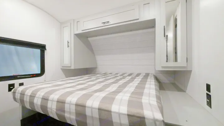 Spacious RV rental bedroom featuring a cozy plaid bed, ample storage via cabinets, and a window for natural light.. Forest River Wildwood 2022