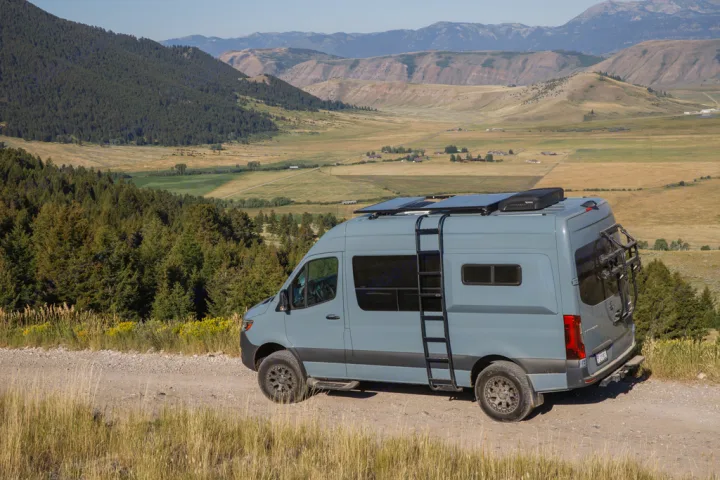 A grey camper van (rv rental) with solar panels on a dirt road, overlooking a vast valley and distant mountains.. Mercedes Sprinter 2021
