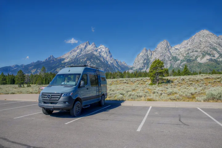 A grey RV rental van, a Mercedes Sprinter, parked in a scenic mountain lot, ready for adventure under a clear sky.. Mercedes Sprinter 2021