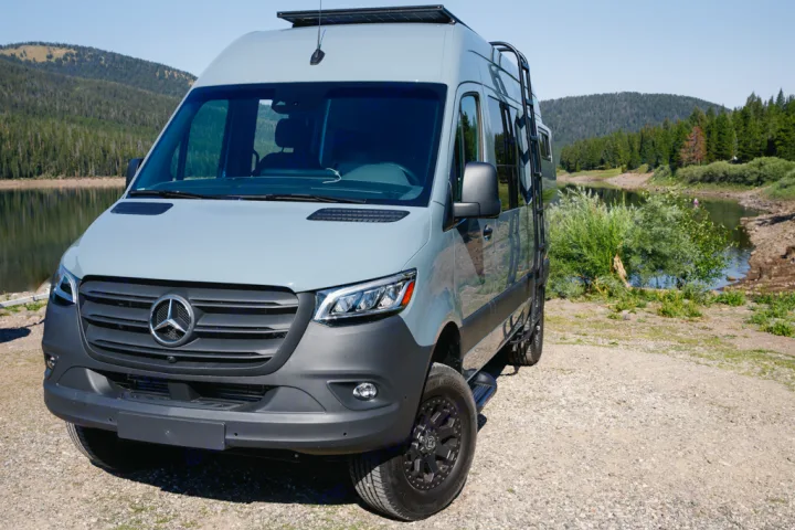 Gray Mercedes-Benz Sprinter camper van by a lake with mountains, perfect for an RV rental adventure.. Mercedes Sprinter 2021