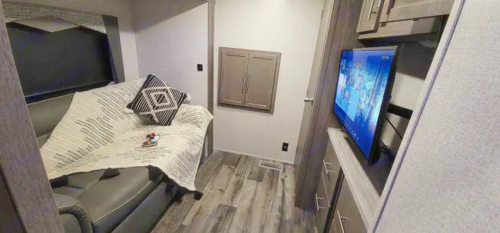 Inside a cozy RV rental: living area with a comfy sofa, patterned blanket, and wall-mounted TV.. Crossroads RV Volante HP 2022