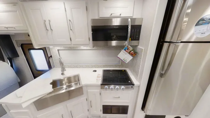 Bright RV rental kitchen with white cabinets, stainless steel fridge, microwave, stove, and sink. Compact and functional.. Coachmen Encore 2021