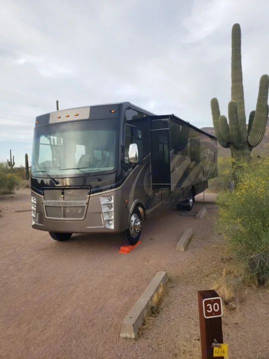 Class A RV rental parked in a desert campsite with saguaro cacti. Orange leveling blocks and site #30 visible.. Coachmen Encore 2021