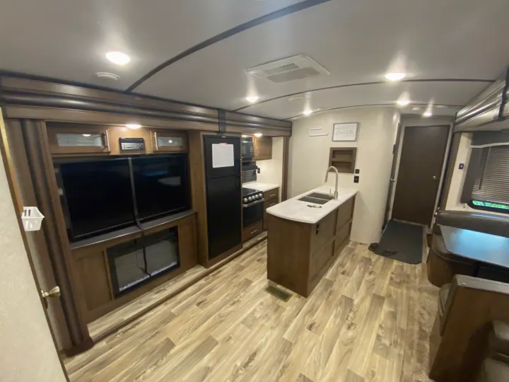 Spacious rv rental interior: modern kitchen island, living area with TV/fireplace, and cozy dinette. Light wood-look floors.. Keystone Cougar Half-Ton 2021