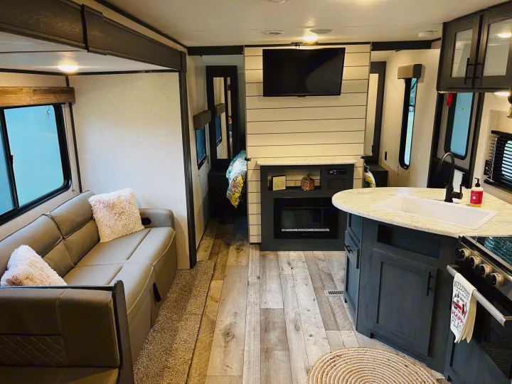 Modern rv rental interior: Comfortable living space with sofa, TV, fireplace, and full kitchen for your next adventure.. Dutchmen Aspen Trail LE 2023