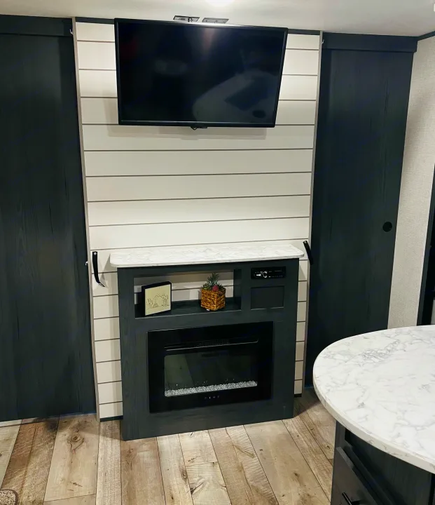 Modern RV living space featuring a white shiplap wall, mounted TV, electric fireplace, and dark built-in cabinets, ideal for an rv rental.. Dutchmen Aspen Trail LE 2023