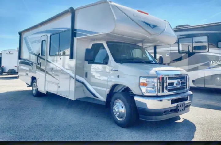Explore in comfort with this light-colored Class C RV rental, featuring a spacious over-cab bunk, perfect for camping and travel.. Coachmen Leprechaun 2022