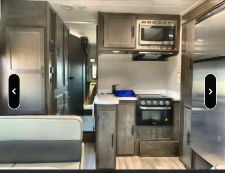 RV rental interior: A modern kitchen area with a microwave, stove/oven, sink, refrigerator, and dinette seating.. Coachmen Leprechaun 2022
