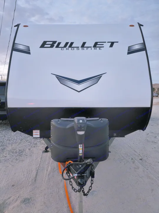 Front view of a sleek, white Bullet Crossfire travel trailer, ideal for your next rv rental adventure, showing its hitch and tanks.. Keystone RV Bullet Crossfire 2022