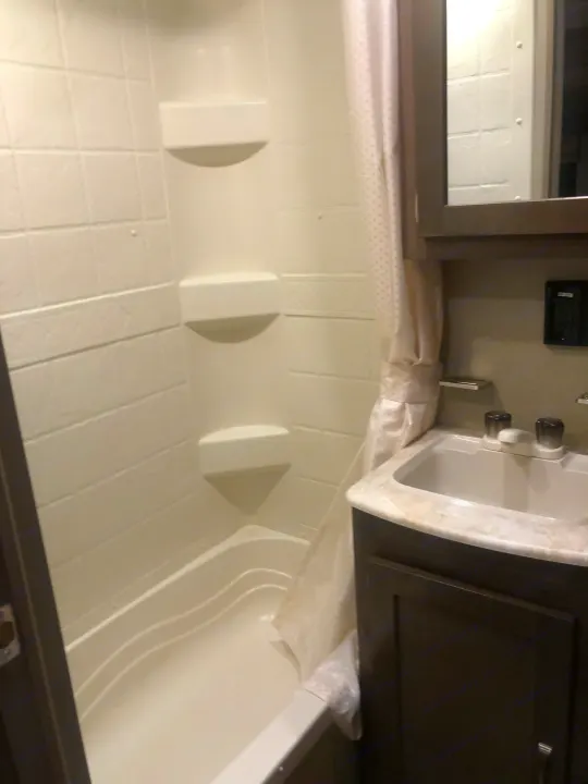 Inside an RV rental bathroom featuring a white tub/shower combo, sink vanity, and mirror cabinet.. Forest River Palomino Puma 2018