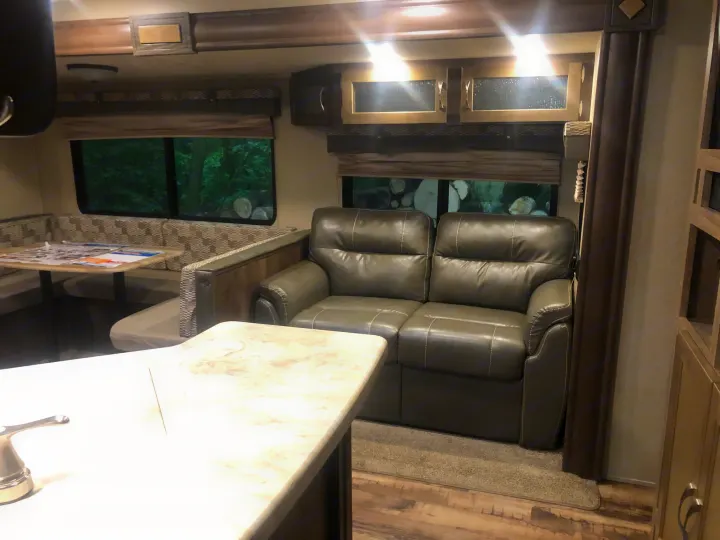 RV rental interior: A spacious living area with a comfortable reclinable sofa, dining booth, and windows showcasing a forest view.. Forest River Palomino Puma 2018