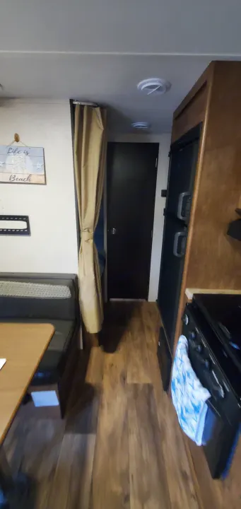 Inside an RV rental: a cozy dinette, kitchen area with fridge and stove, a door, and warm wood-look flooring.. Forest River Salem Cruise Lite 2018