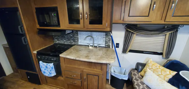 RV rental interior featuring a compact kitchen with stove, sink, microwave, and adjacent living area seating.. Forest River Salem Cruise Lite 2018