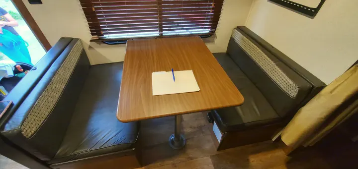 **RV rental** dinette booth: dark benches with patterned backs, a wooden table, and a pen/folder.. Forest River Salem Cruise Lite 2018