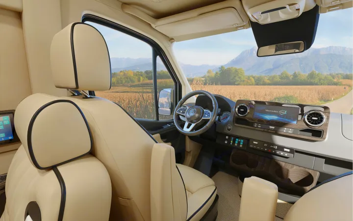 Modern RV rental interior: cream seats, Mercedes dashboard, and a scenic view of mountains and fields.. Ultimate Toys Ultimate Cruiser 2022