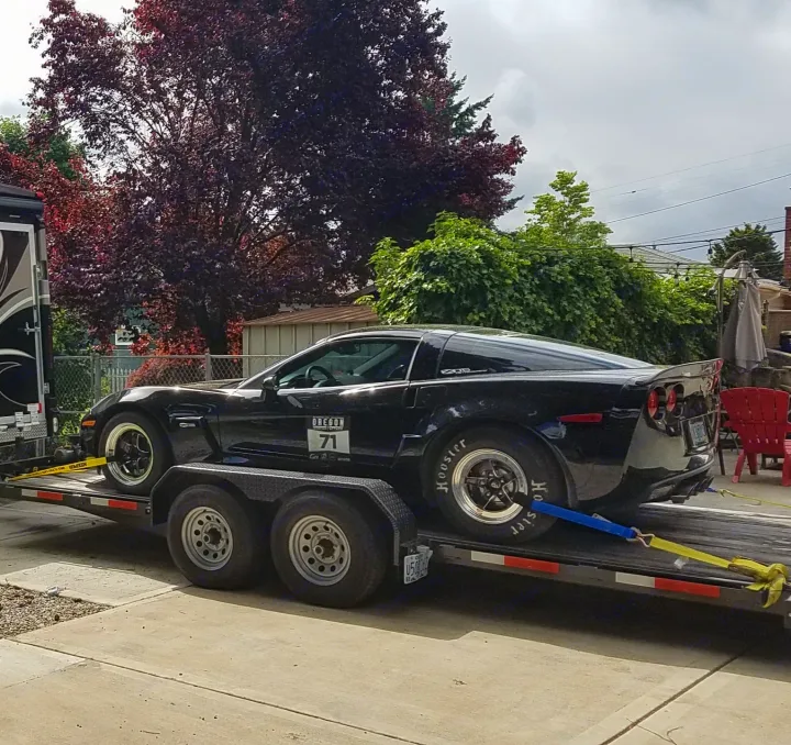 A black C6 Corvette drag car on a trailer, hitched to an RV rental, ready for the track.. Eagle flatbed 2019