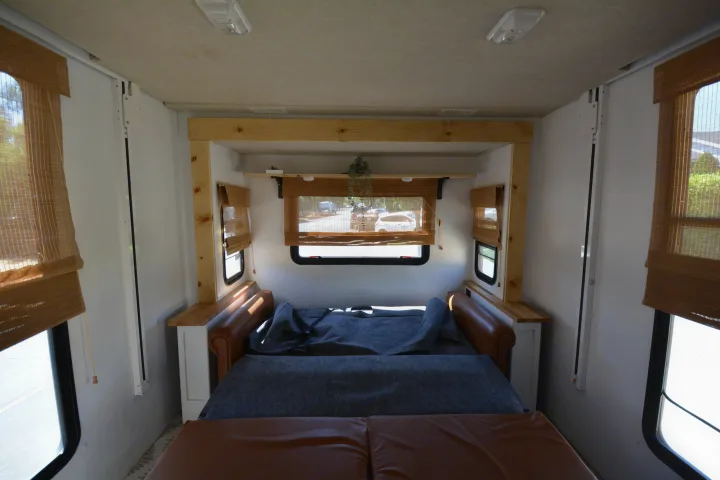 Inside an RV rental: a cozy space with a brown couch/bed, wooden details, and bamboo blinds on the windows.. Jamboree Sport 2011