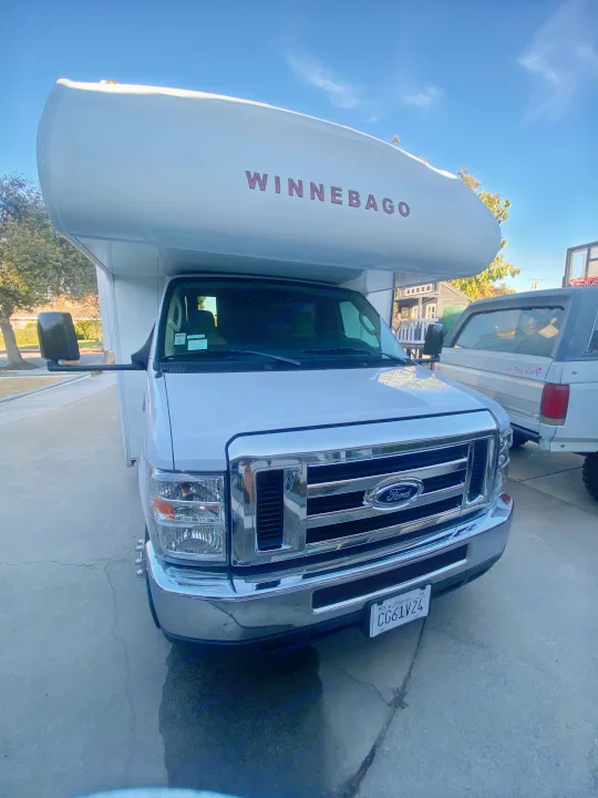 Front view of a white Winnebago RV rental, a Ford Class C motorhome, parked on a driveway under clear skies.. Winnebago Outlook 2019