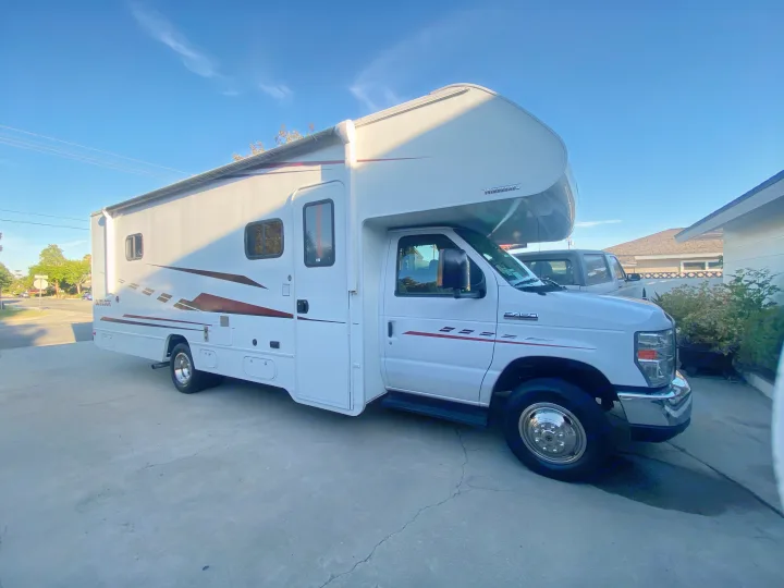 White Class C Winnebago RV rental parked on a driveway. Sunny day, clear sky, ready for adventure.. Winnebago Outlook 2019
