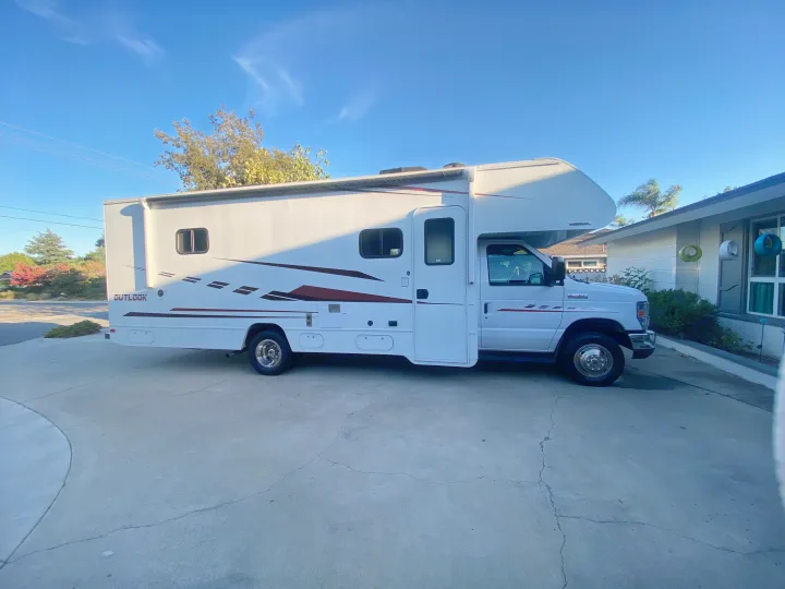 White Winnebago Outlook RV rental parked on a paved driveway under a clear blue sky.. Winnebago Outlook 2019