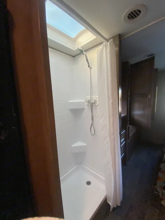 Inside an RV rental: a clean, bright shower with a skylight and handheld showerhead, complete with white curtain.. Winnebago Outlook 2019
