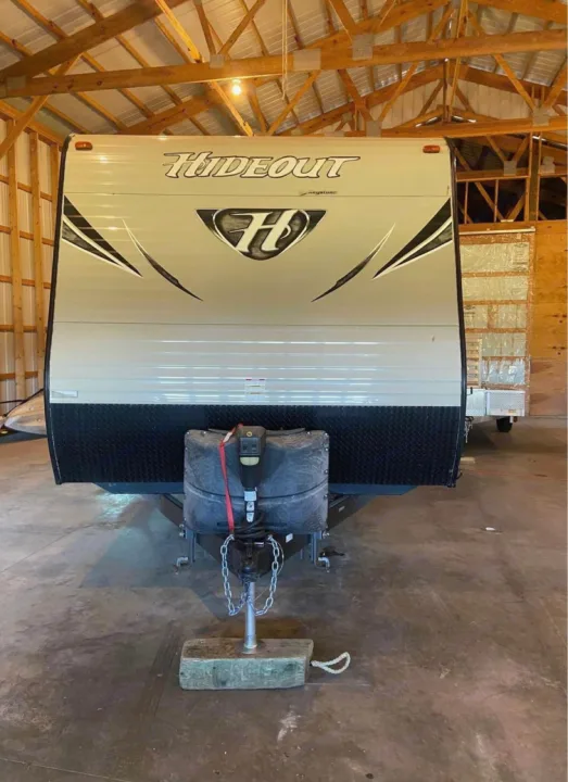 Front view of an RV rental: a light-colored Hideout travel trailer with black lower panel, parked indoors.. Keystone Hideout 2016