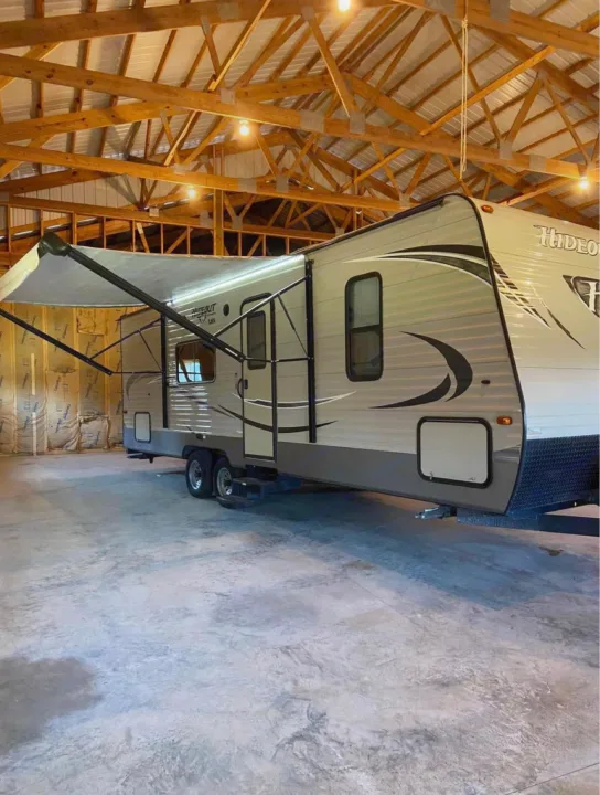 Travel trailer RV rental in a spacious garage with wooden beams. Awning extended, well-lit concrete floor.. Keystone Hideout 2016