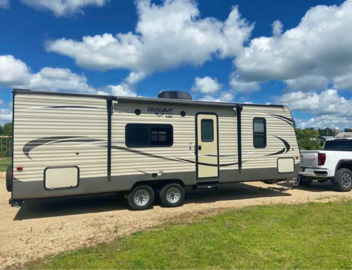 Spacious travel trailer RV rental, towed by a pickup truck, ready for outdoor adventures under sunny skies.. Keystone Hideout 2016