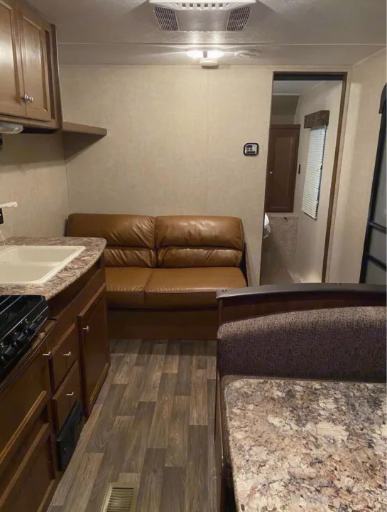RV rental interior: a compact living space with a kitchen, brown sofa, and dinette, featuring wood-look flooring.. Keystone Hideout 2016