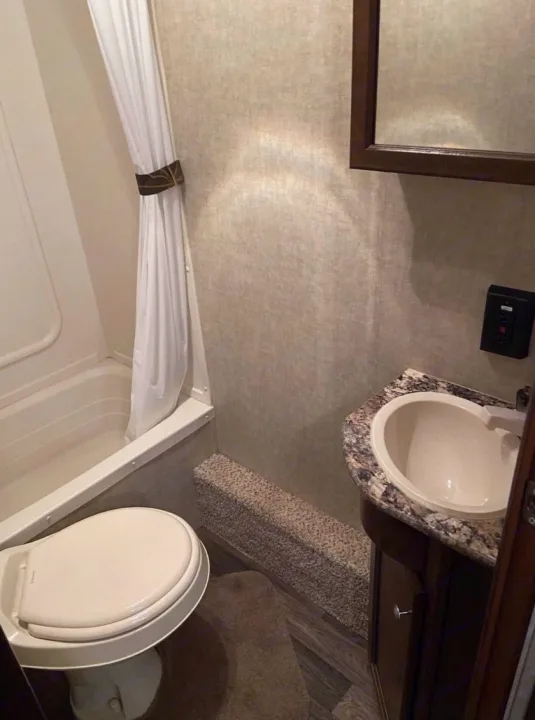 Compact RV rental bathroom with tub, toilet, sink, and mirror. Features a carpeted step and efficient layout for travel.. Keystone Hideout 2016