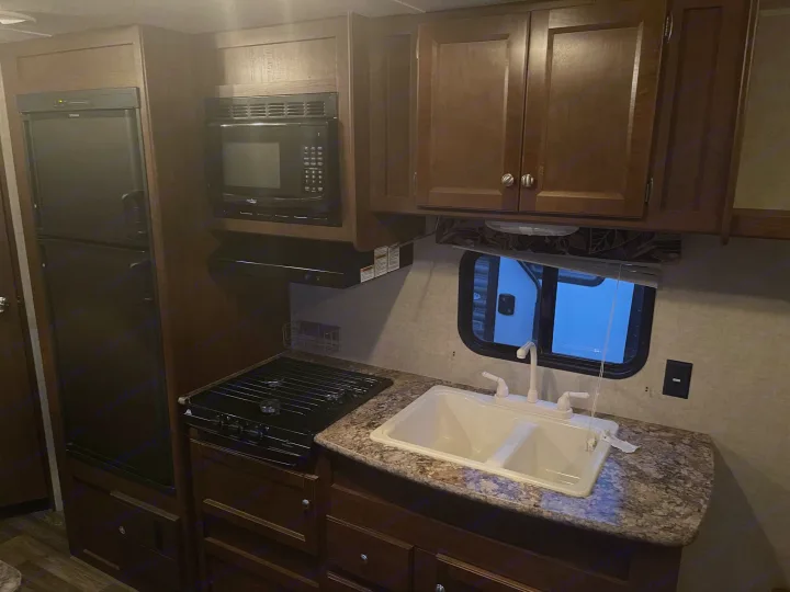 RV rental kitchen, featuring a refrigerator, microwave, gas range, double sink, and wooden cabinetry.. Keystone Hideout 2016