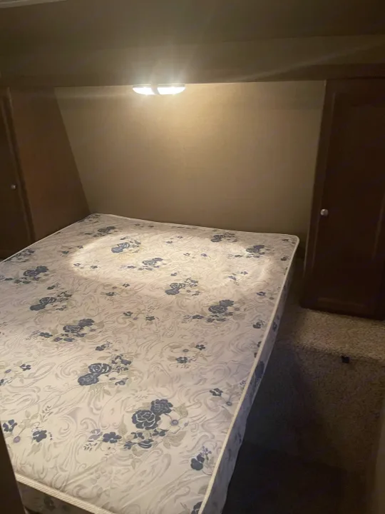 Compact RV rental bedroom with floral mattress, built-in storage, and overhead light for a comfortable stay.. Keystone Hideout 2016