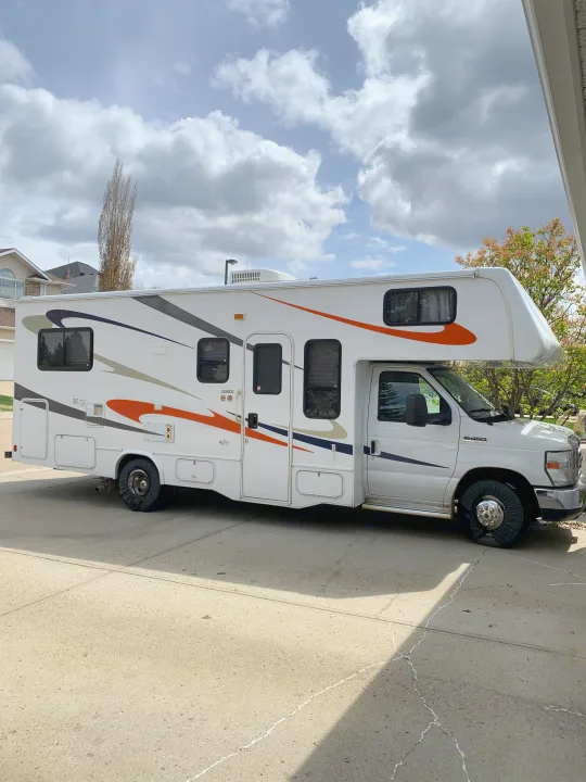 White Class C RV rental, with tire covers, parked on a paved driveway under a cloudy sky.. Forester Forester Motorhome 2010