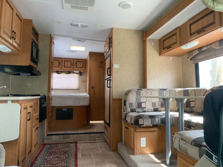 Experience comfort in this rv rental. View of kitchen, dinette, and cozy bed area with wood cabinets & tile flooring.. Forester Forester Motorhome 2010