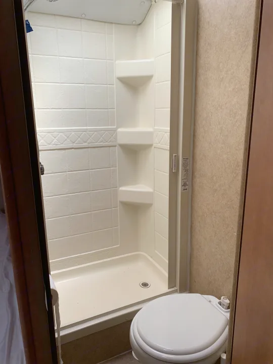 Compact RV rental bathroom with a white enclosed shower stall, built-in shelves, and a toilet.. Forester Forester Motorhome 2010