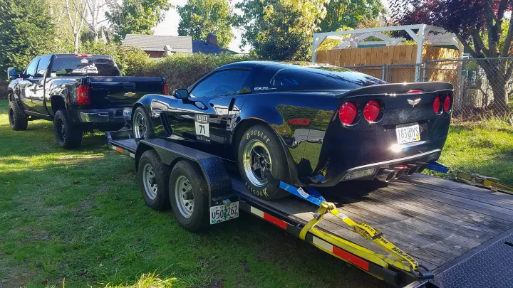 Powerful black truck towing a black Corvette race car on a trailer. Ready for track days, much like an RV rental for travel.. Eagle flatbed 2019