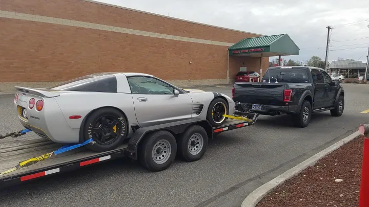 Black Ford Raptor hauling a Corvette race car on a trailer. This powerful setup beats an rv rental for track adventures.. Eagle flatbed 2019