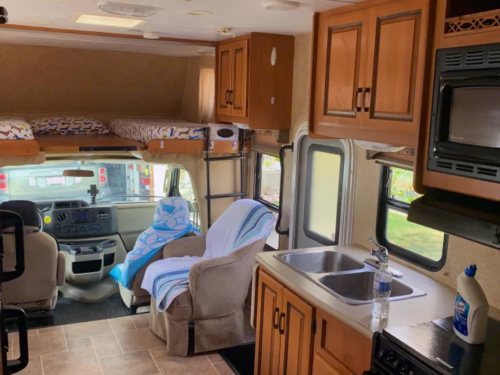 Bright rv rental interior with overhead beds, kitchenette, driver's seats, and cozy chairs.. Forester Forester Motorhome 2010