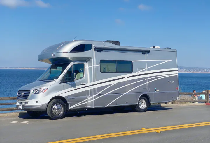 A sleek gray Winnebago View RV (possibly an rv rental) parked by the ocean under a clear blue sky. Ideal for a scenic road trip.. Winnebago View 2022