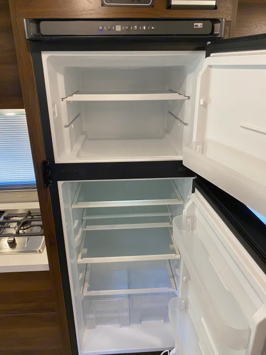 Open, clean two-door RV rental refrigerator & freezer, showing empty shelves, ready for your travel adventures.. Winnebago View 2022