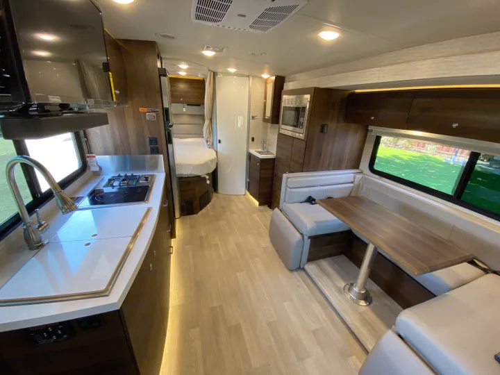 Spacious RV rental interior featuring a full kitchen, dining area with booth seating, and a rear sleeping area. Modern design.. Winnebago View 2022