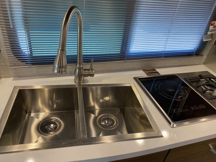Compact rv rental kitchen: Stainless steel double sink, modern faucet, and sleek induction/gas cooktop on a white counter.. Winnebago View 2022