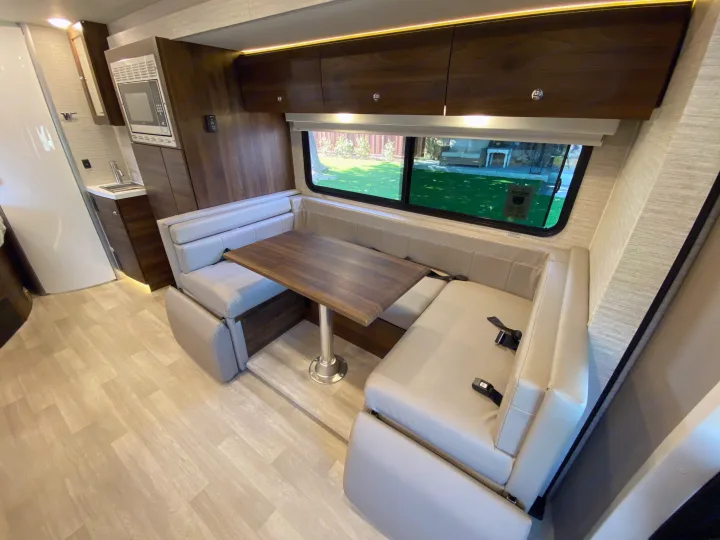 Modern RV rental interior: bright dinette seating, wood table, and compact kitchenette with sink and microwave.. Winnebago View 2022